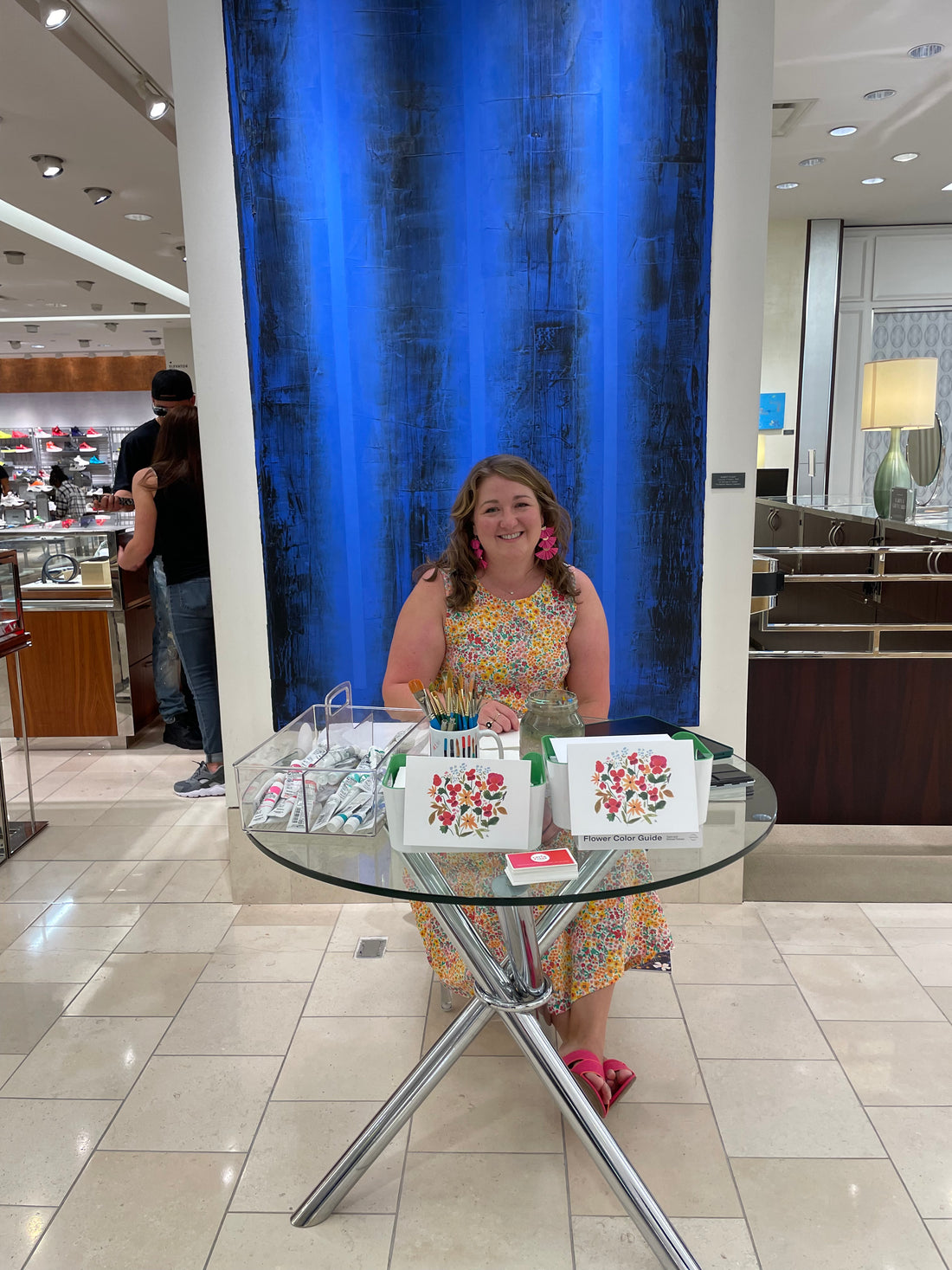 Tiffani Evans seated at table live painting in Neiman Marcus Southpark Mall